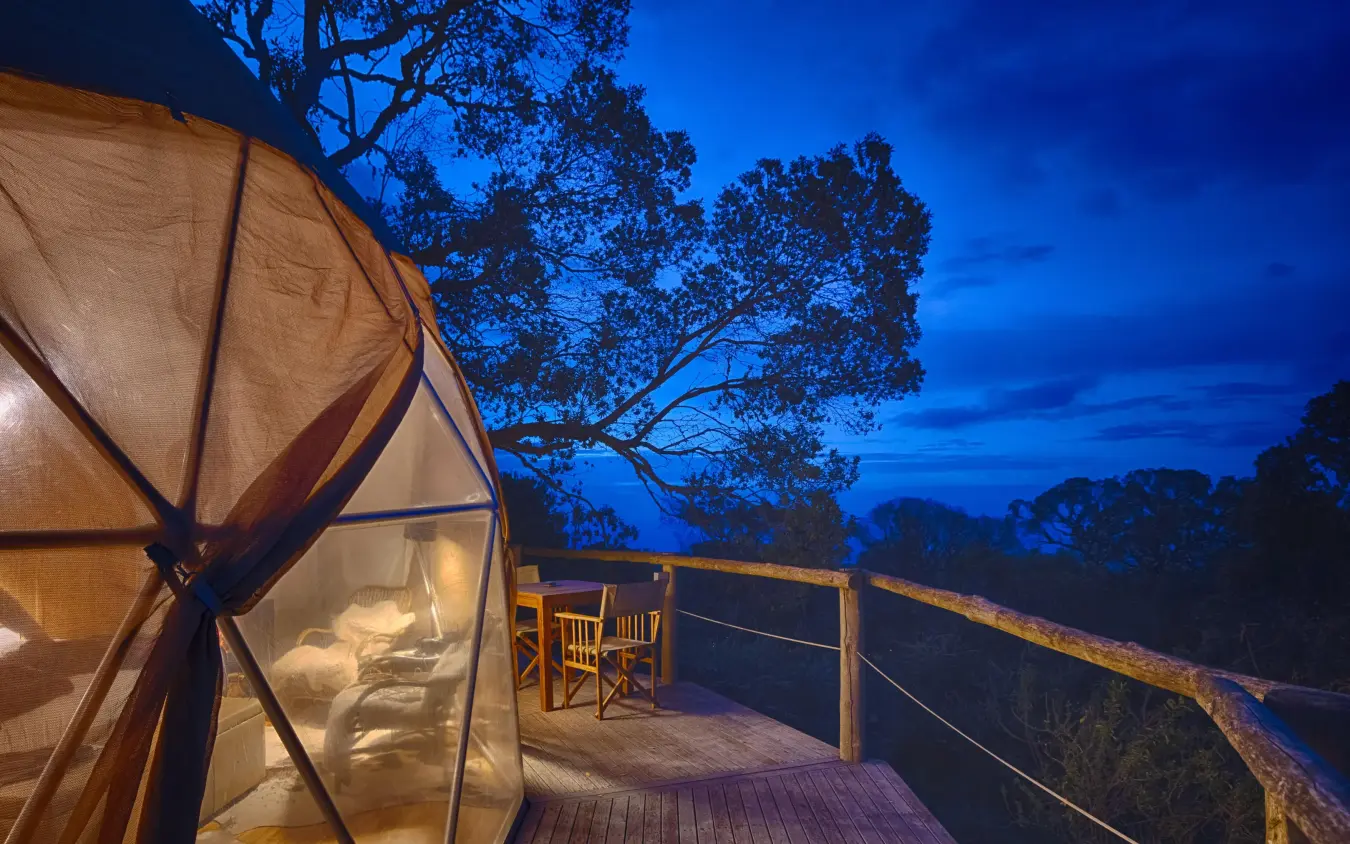 Illuminated glamping tent on wooden deck at dusk, The Highlands, Ngorongoro Crater, Tanzania