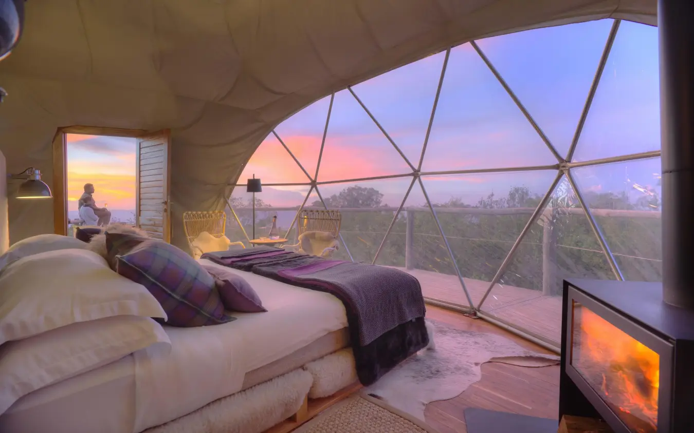 Bedroom interior with panoramic windows overlooking sunset landscape, The Highlands, Ngorongoro Crater, Tanzania