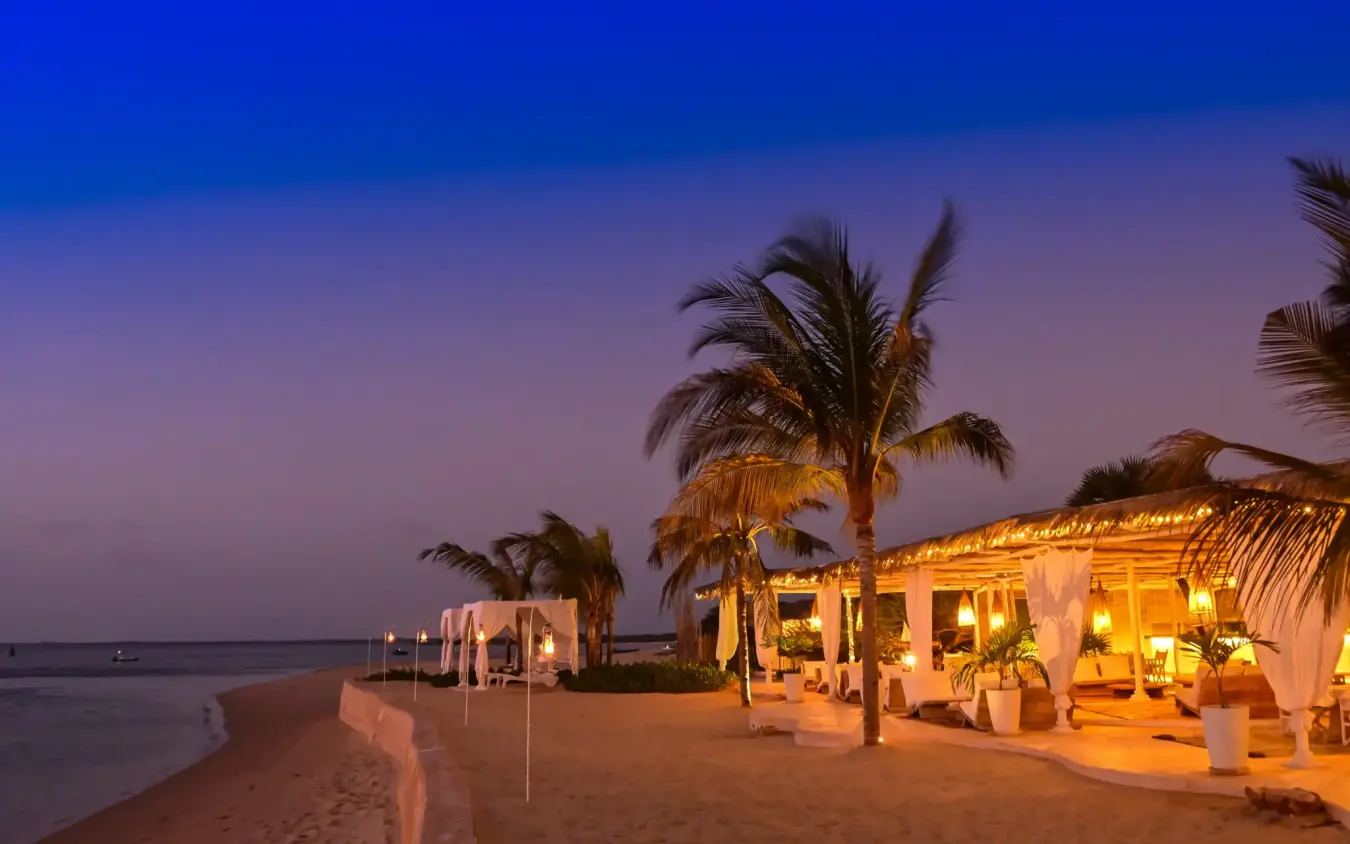 Beach pavilions illuminated at dusk with palm trees, The Majlis Resort, Lamu Archipelago, Kenya