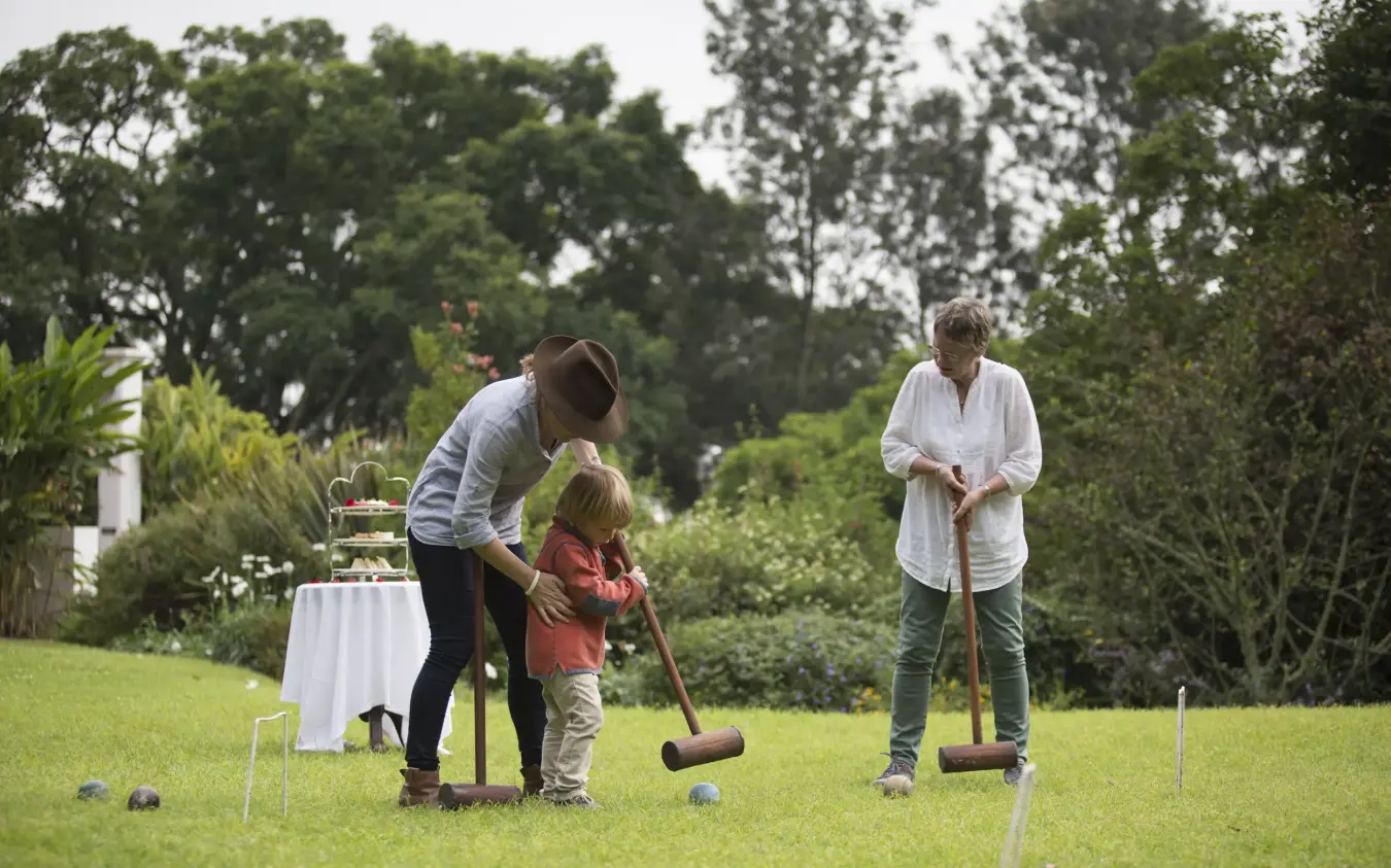 Family playing croquet on manicured lawn with garden and trees, The Manor at Ngorongoro, Ngorongoro Crater, Tanzania