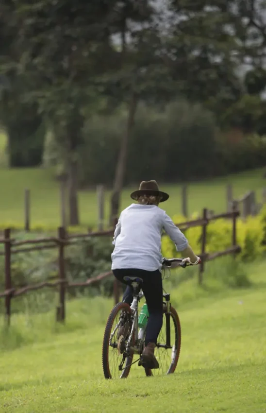 Person cycling through grassy parkland with rustic wooden fencing, The Manor at Ngorongoro, Ngorongoro Crater, Tanzania