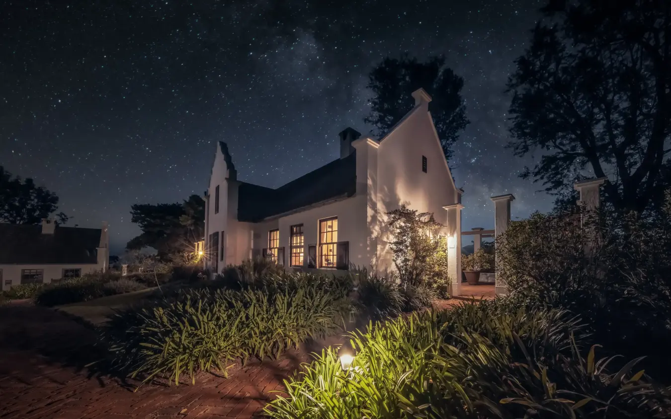Illuminated white farmhouse under starry night sky with manicured gardens, The Manor at Ngorongoro, Ngorongoro Crater, Tanzania