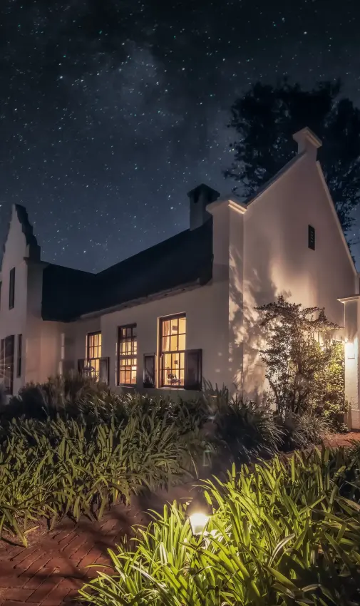 Illuminated white farmhouse under starry night sky with manicured gardens, The Manor at Ngorongoro, Ngorongoro Crater, Tanzania