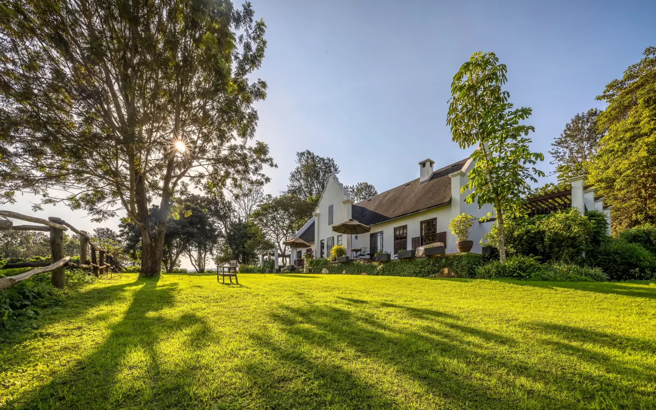 White farmhouse with thatched roof on manicured lawn with mature trees, The Manor at Ngorongoro, Ngorongoro Crater, Tanzania