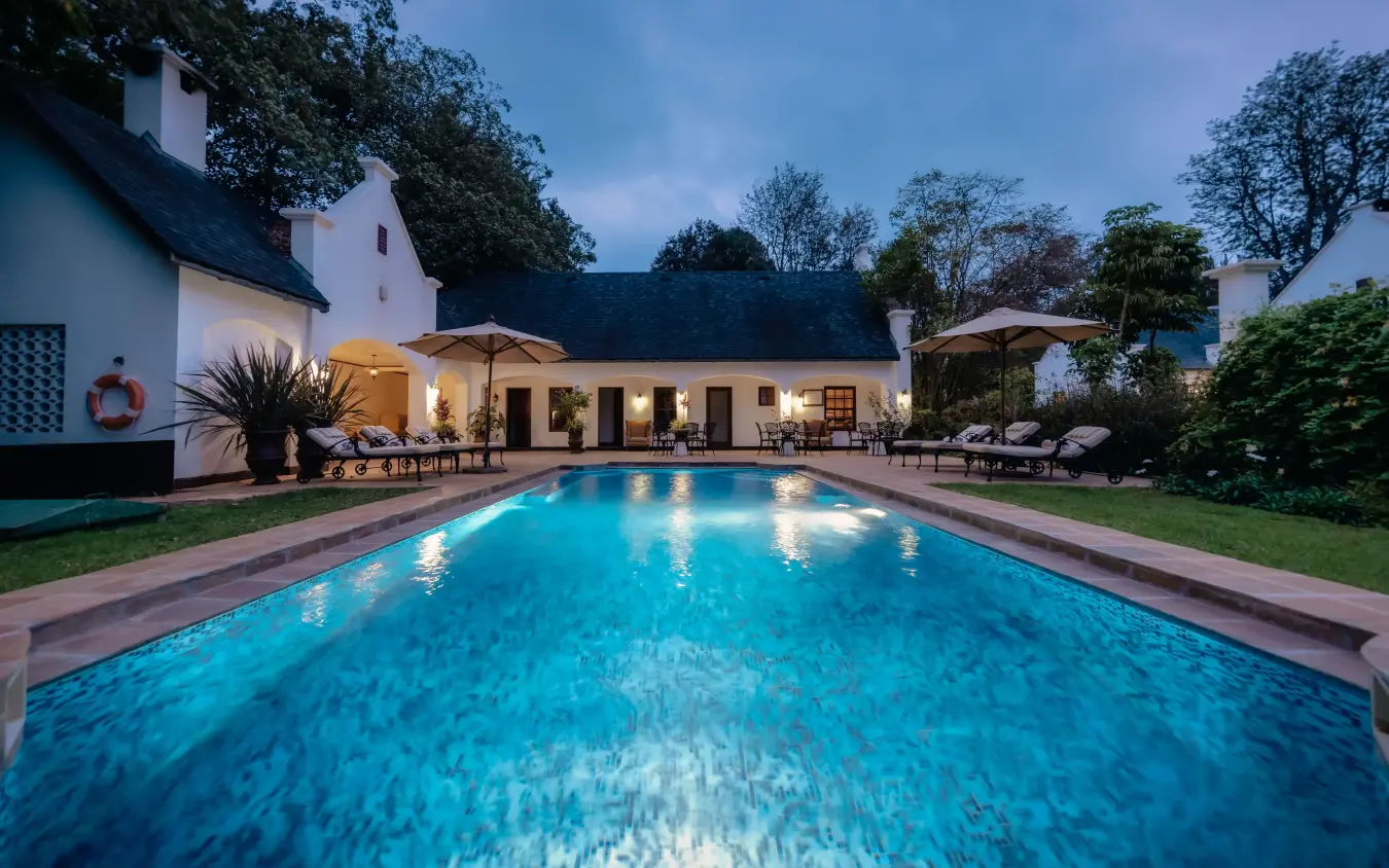 Illuminated swimming pool with colonial-style lodge at dusk, The Manor at Ngorongoro, Ngorongoro Crater, Tanzania