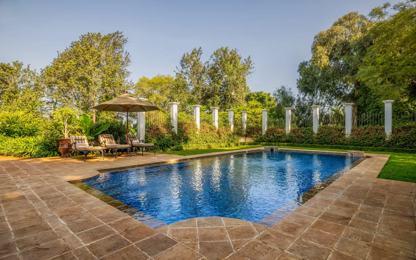 Rectangular swimming pool with white columns and lounge chairs in manicured garden, The Manor at Ngorongoro, Ngorongoro Crater, Tanzania
