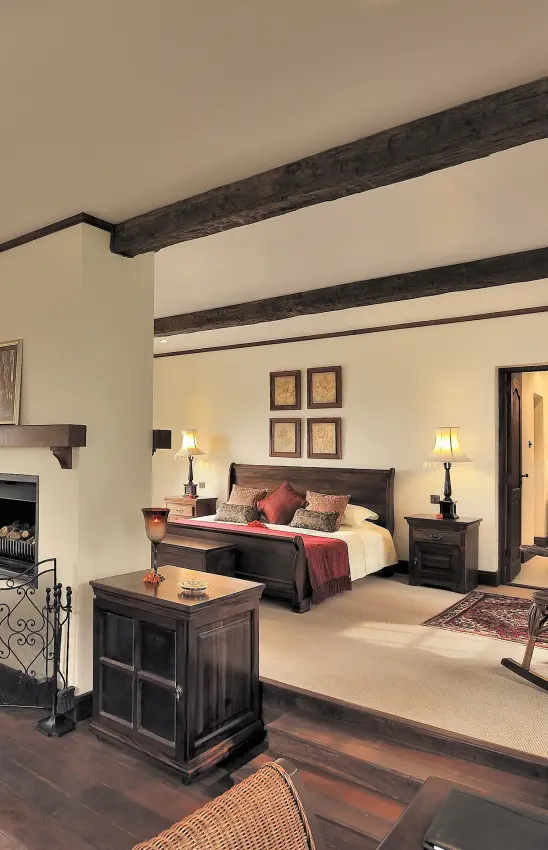 Bedroom with exposed dark wooden beams and fireplace, The Manor at Ngorongoro, Ngorongoro Crater, Tanzania