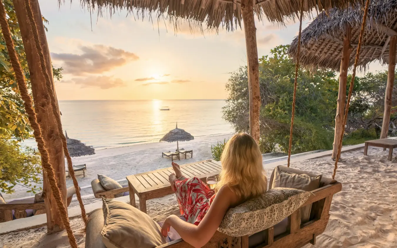 Woman relaxing on beach deck at sunset overlooking ocean, The Manta Resort, Zanzibar & Pemba, Tanzania
