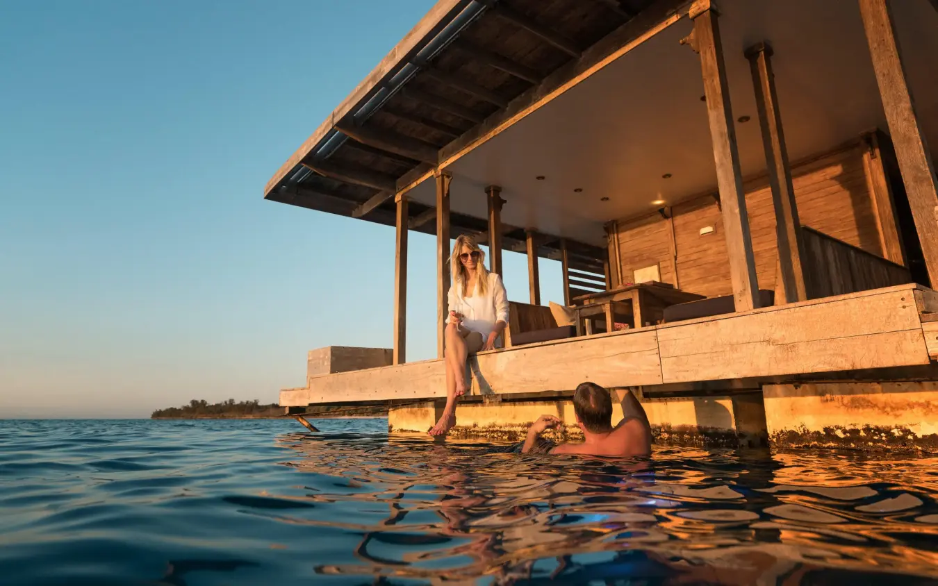 Guests relaxing on wooden deck at sunset over water, The Manta Resort, Zanzibar & Pemba, Tanzania