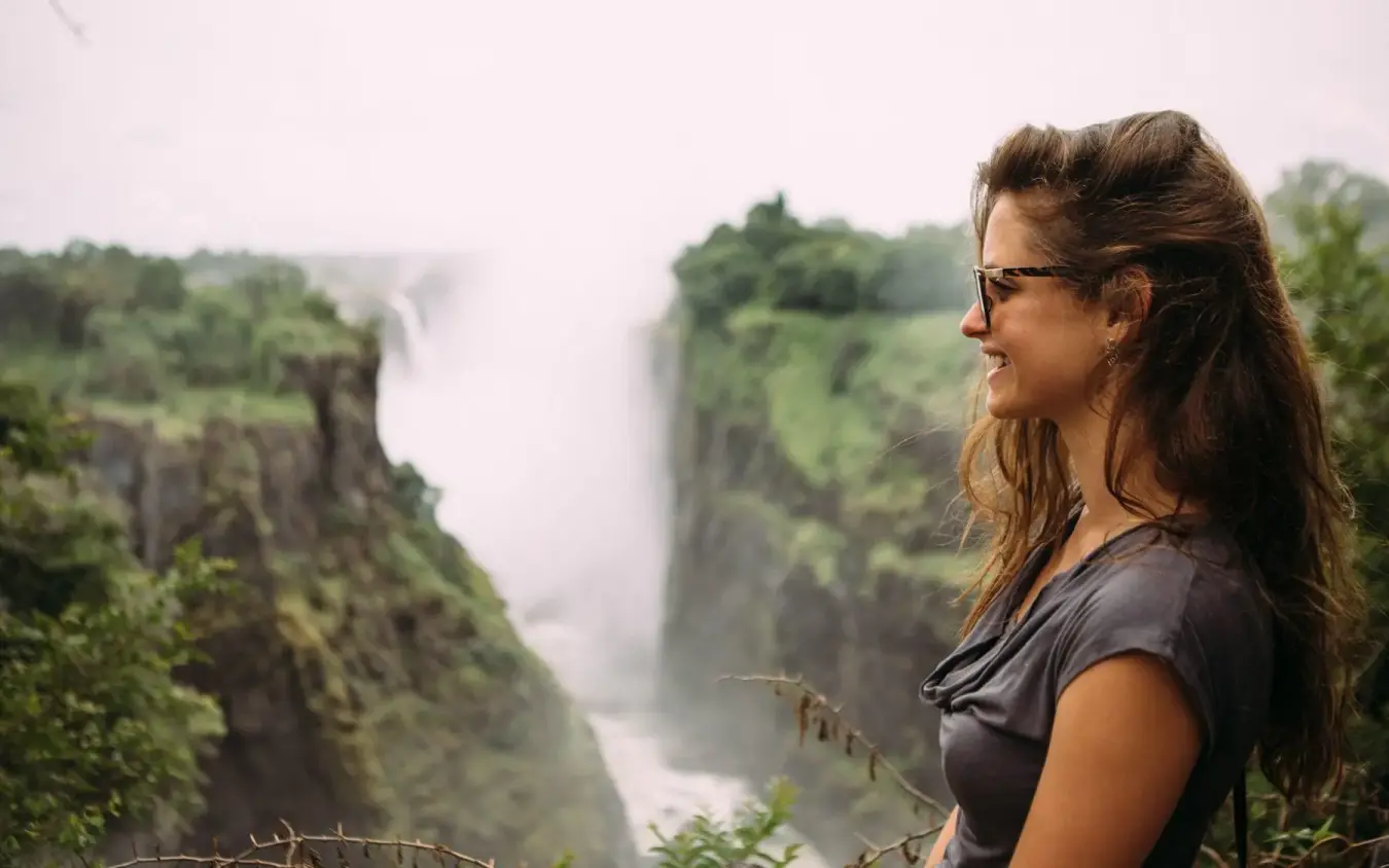 Woman overlooking vast gorge with waterfall and green vegetation, The Wallow Lodge, Hwange National Park, Zimbabwe