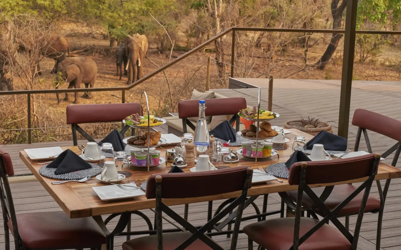 Dining table on wooden deck overlooking elephants, The Wallow Lodge, Hwange National Park, Zimbabwe