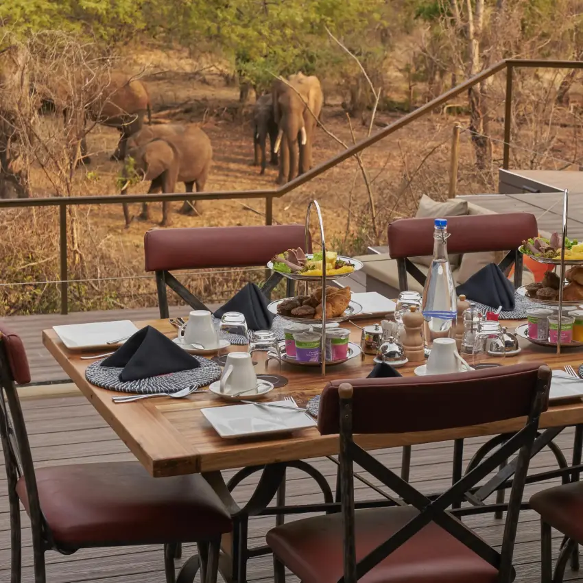 Dining table on wooden deck overlooking elephants, The Wallow Lodge, Hwange National Park, Zimbabwe