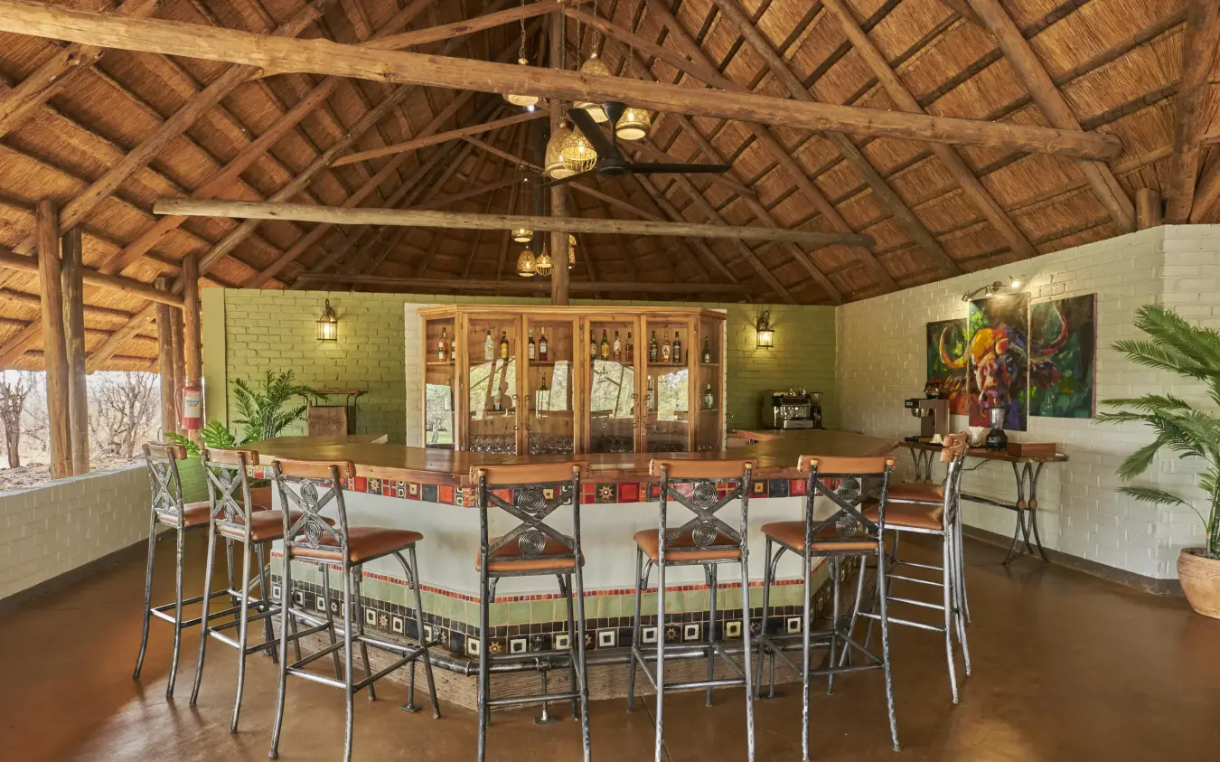 Open-air bar lounge with wooden beam ceiling and bar seating, The Wallow Lodge, Hwange National Park, Zimbabwe