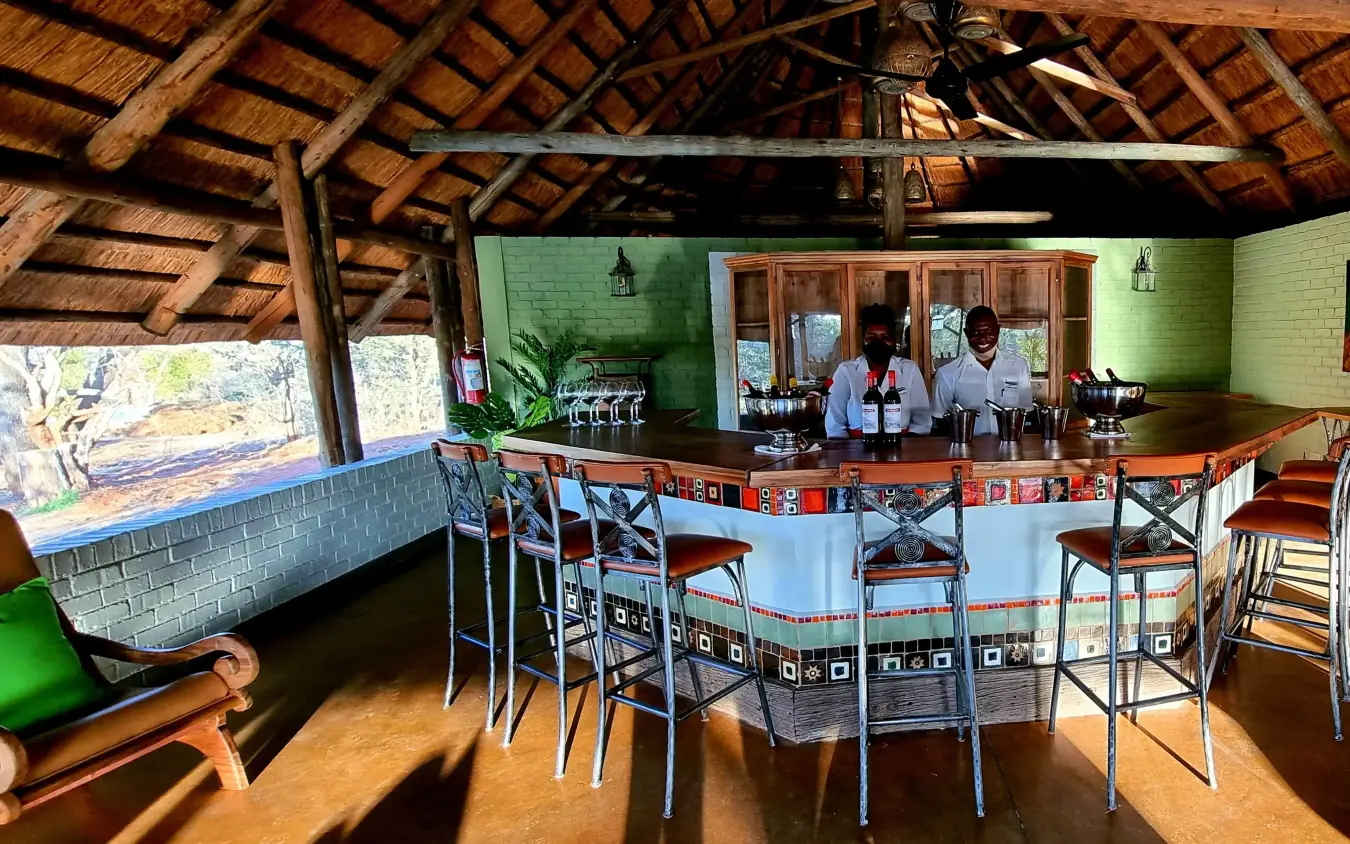 Open-air bar and lounge with green walls and wooden beams, The Wallow Lodge, Hwange National Park, Zimbabwe