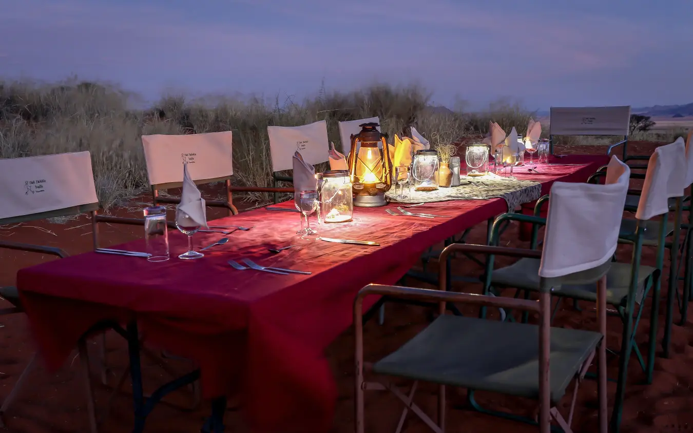 Long outdoor dining table set for dinner at dusk, Tok Tokkie Trails, NamibRand Private Reserve, Namibia