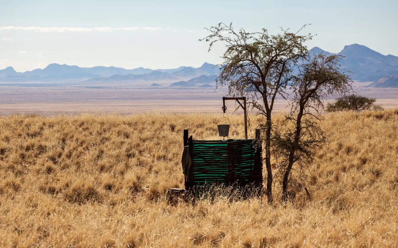 Arid savanna landscape with distant mountains and weathered wooden structure, Tok Tokkie Trails, NamibRand Private Reserve, Namibia