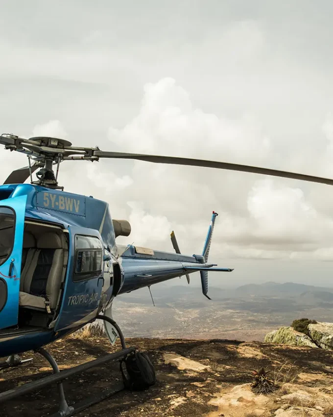 Blue helicopter parked on rocky hilltop with valley landscape below, Samburu Reserve, Kenya