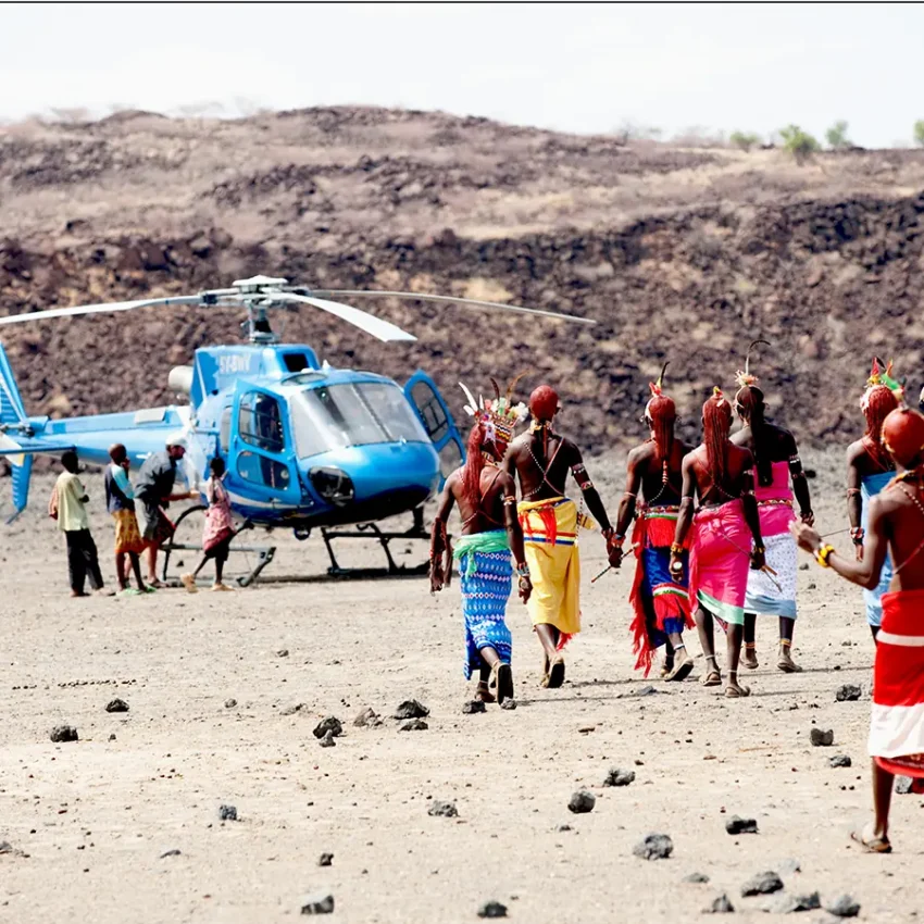 Blue helicopter landing near indigenous community in arid landscape, Samburu Reserve, Kenya