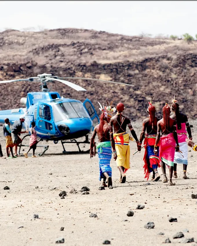 Blue helicopter landing near indigenous community in arid landscape, Northern Kenya, Kenya