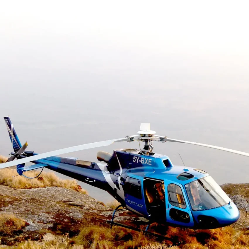Helicopter parked on rocky terrain with dry grassland and overcast sky