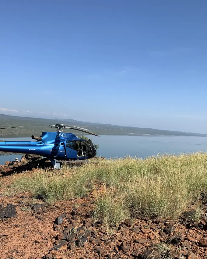Blue helicopter parked on rocky hillside overlooking turquoise lake, Lake Natron, Tanzania