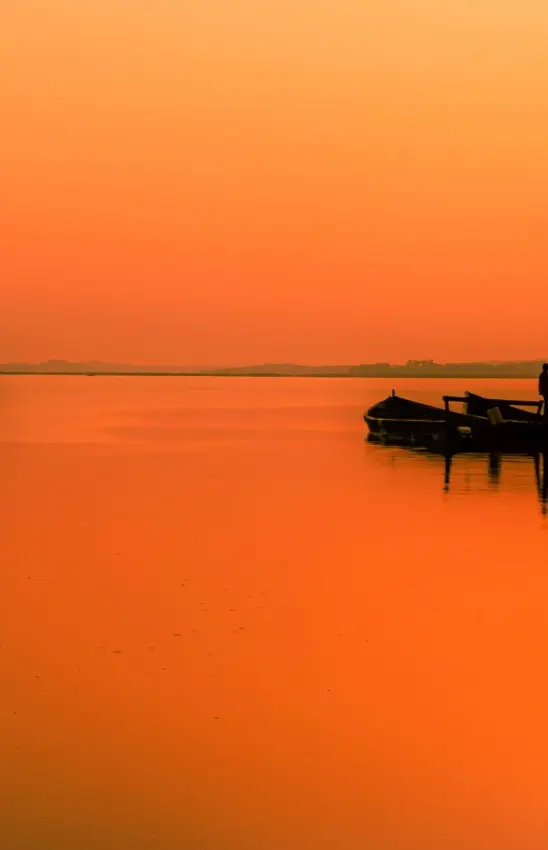Silhouetted fishing boats and dock on a calm Uganda waterway at sunset