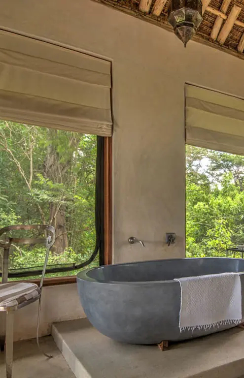 Modern stone bathtub with forest views through large windows, Umani Springs, Amboseli and Chyulu Hills, Kenya