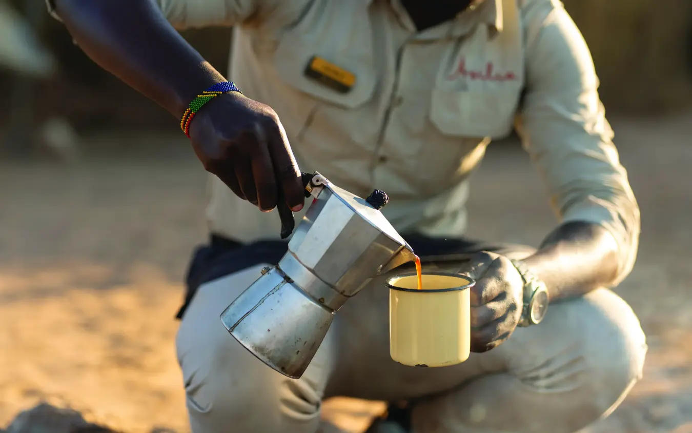 Guide pouring freshly brewed coffee into enamel camp cup, Usangu Expedition Camp, Ruaha National Park, Tanzania