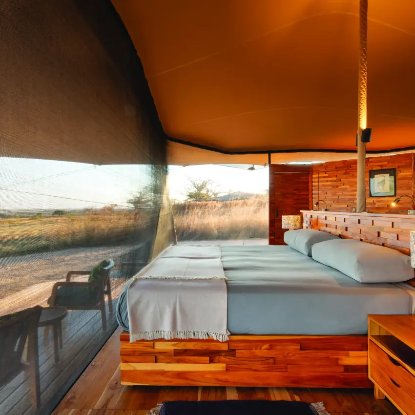 Canvas safari tent bedroom with savanna views through mesh window, Usangu Expedition Camp, Ruaha National Park, Tanzania