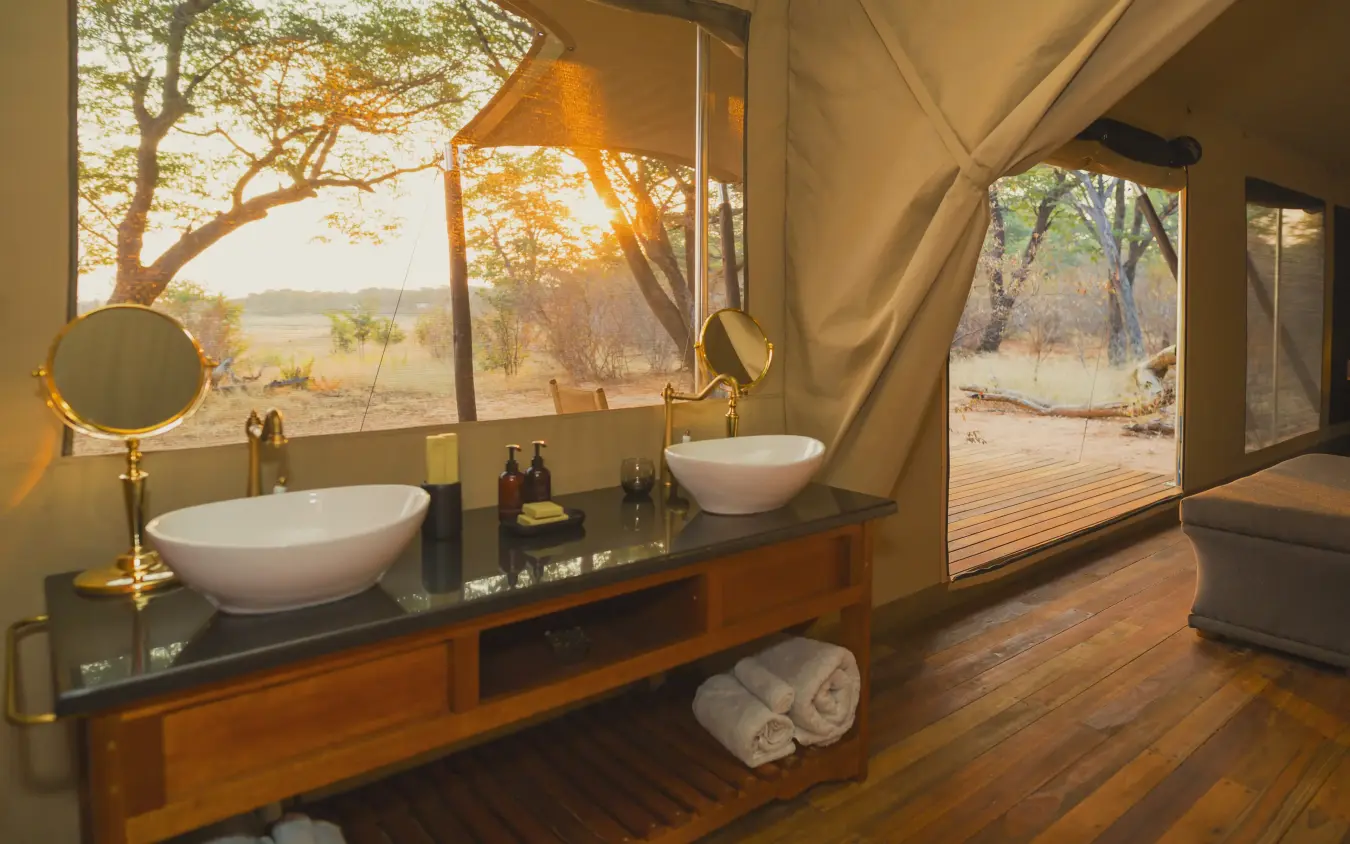 Luxury safari tent bathroom with dual basins overlooking woodland savanna at sunset, Verney’s Camp, Hwange National Park, Zimbabwe