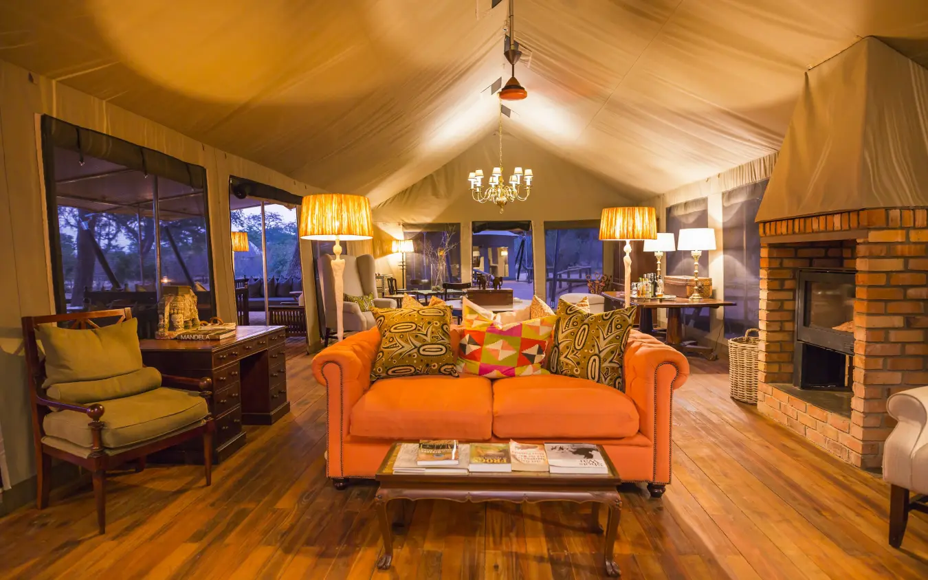 Luxury safari lodge interior with fireplace and orange sofa at dusk, Verney’s Camp, Hwange National Park, Zimbabwe