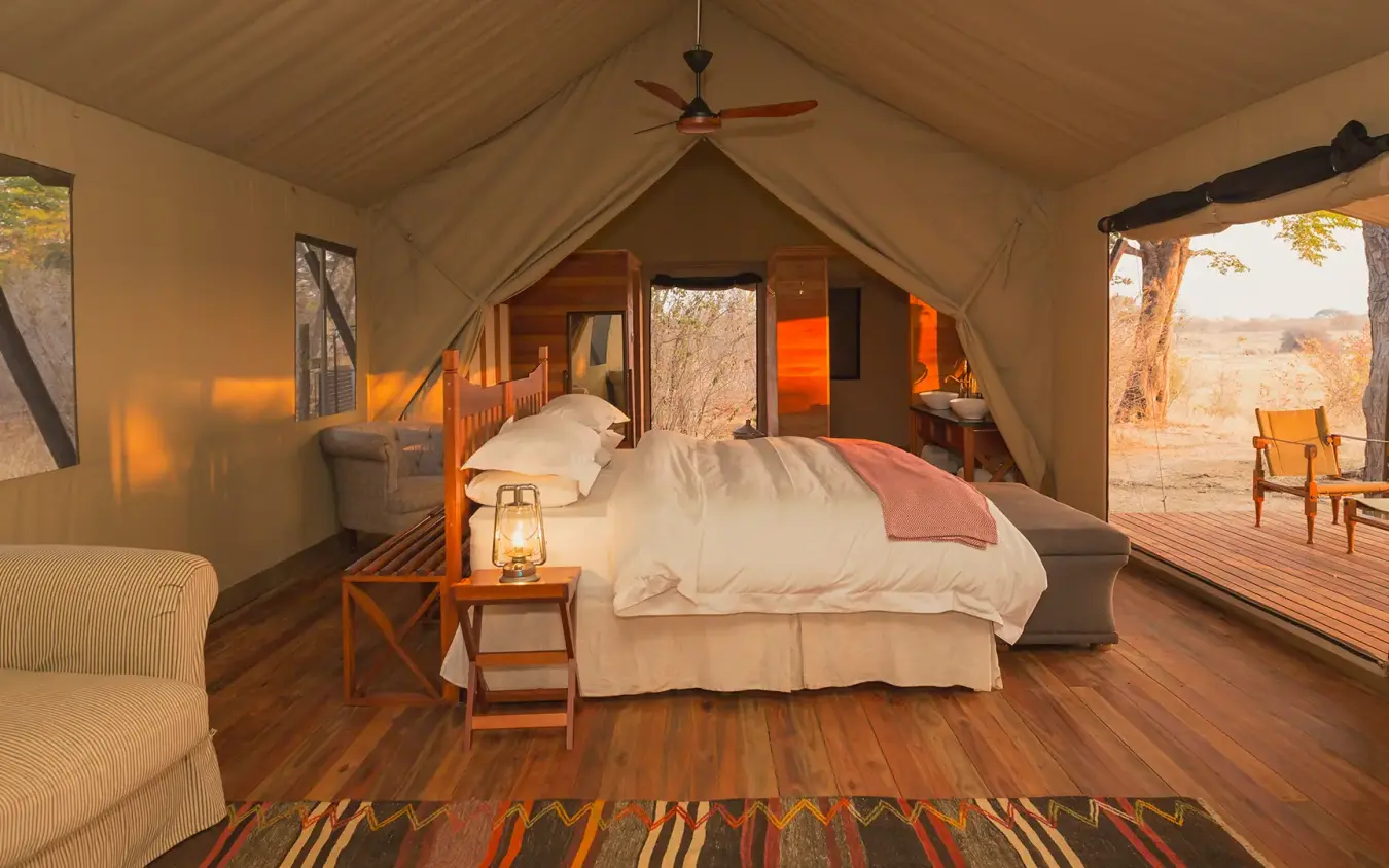 Luxury safari tent bedroom with open deck overlooking savanna landscape at sunset, Verney’s Camp, Hwange National Park, Zimbabwe
