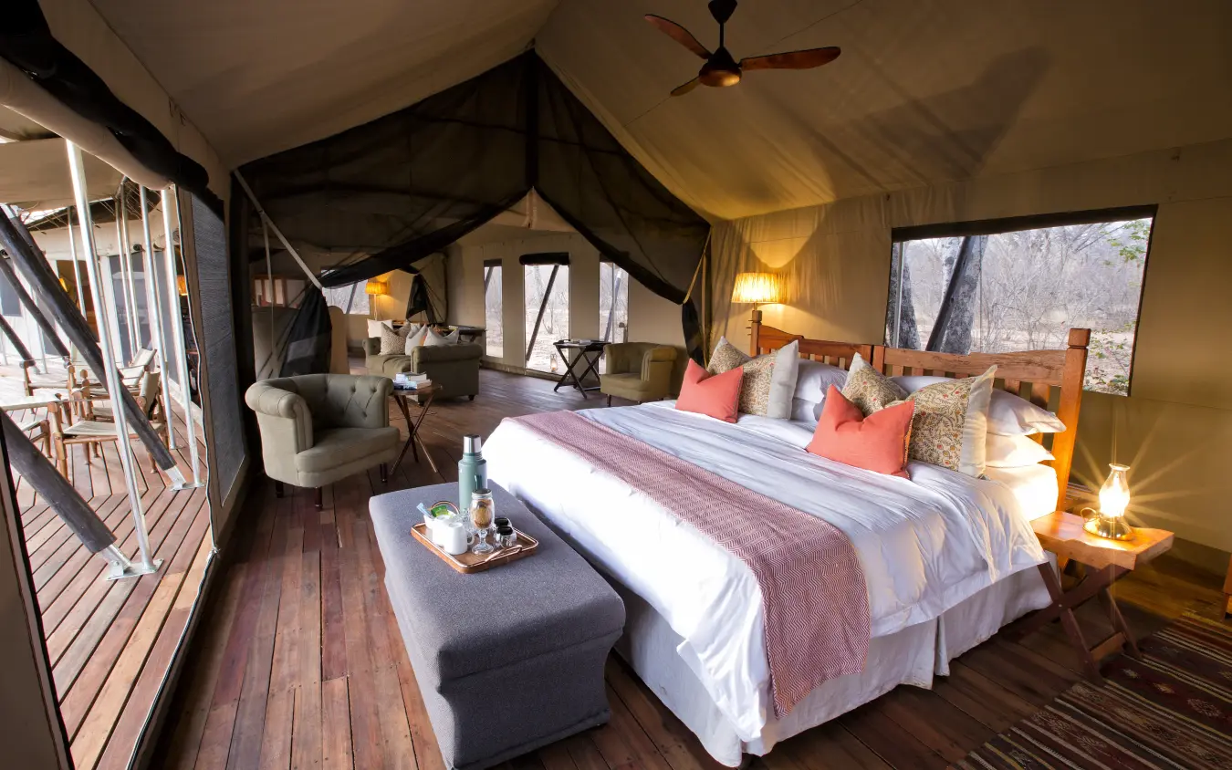 Luxury safari tent bedroom with four-poster bed and wooden deck viewing wildlife area, Verney’s Camp, Hwange National Park, Zimbabwe