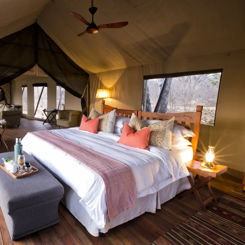 Luxury safari tent bedroom with four-poster bed and wooden deck viewing wildlife area, Verney’s Camp, Hwange National Park, Zimbabwe
