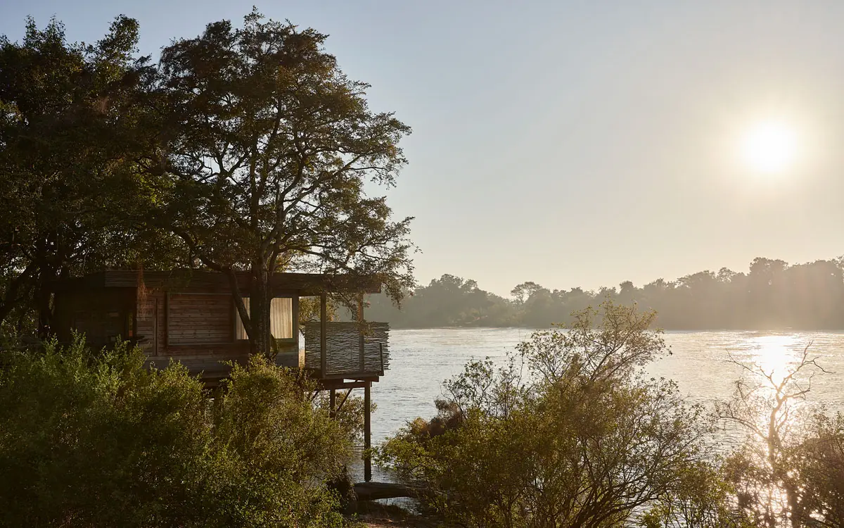 Wooden deck overlooking river at sunrise with trees, Island Treehouse Suites, Victoria Falls, Zimbabwe