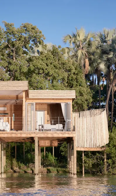 Wooden riverside lodge on stilts surrounded by vegetation, Island Treehouse Suites, Victoria Falls, Zimbabwe