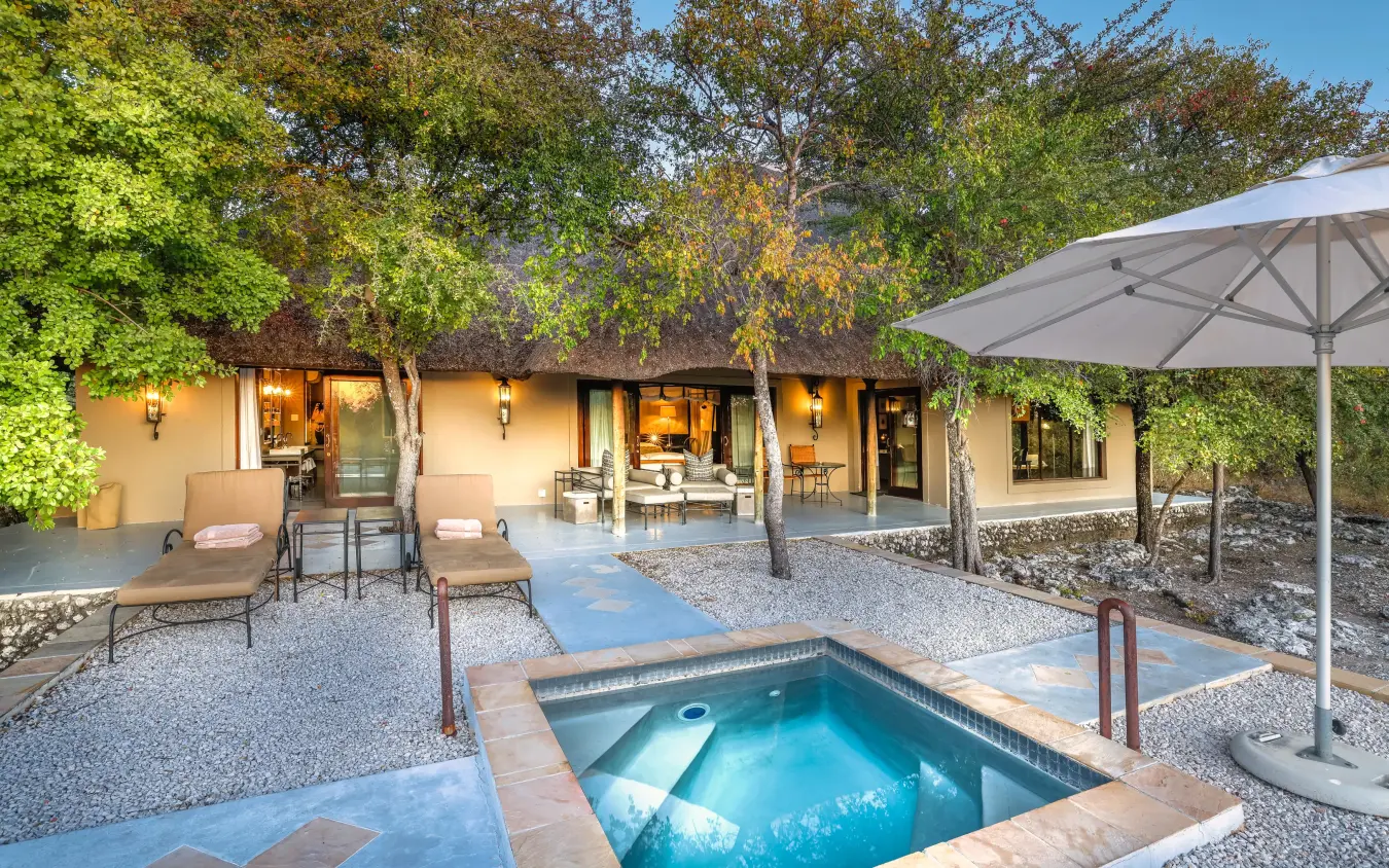 Private pool and lounge area with shade umbrella and illuminated lodge building, Villa Mushara, Etosha National Park, Namibia