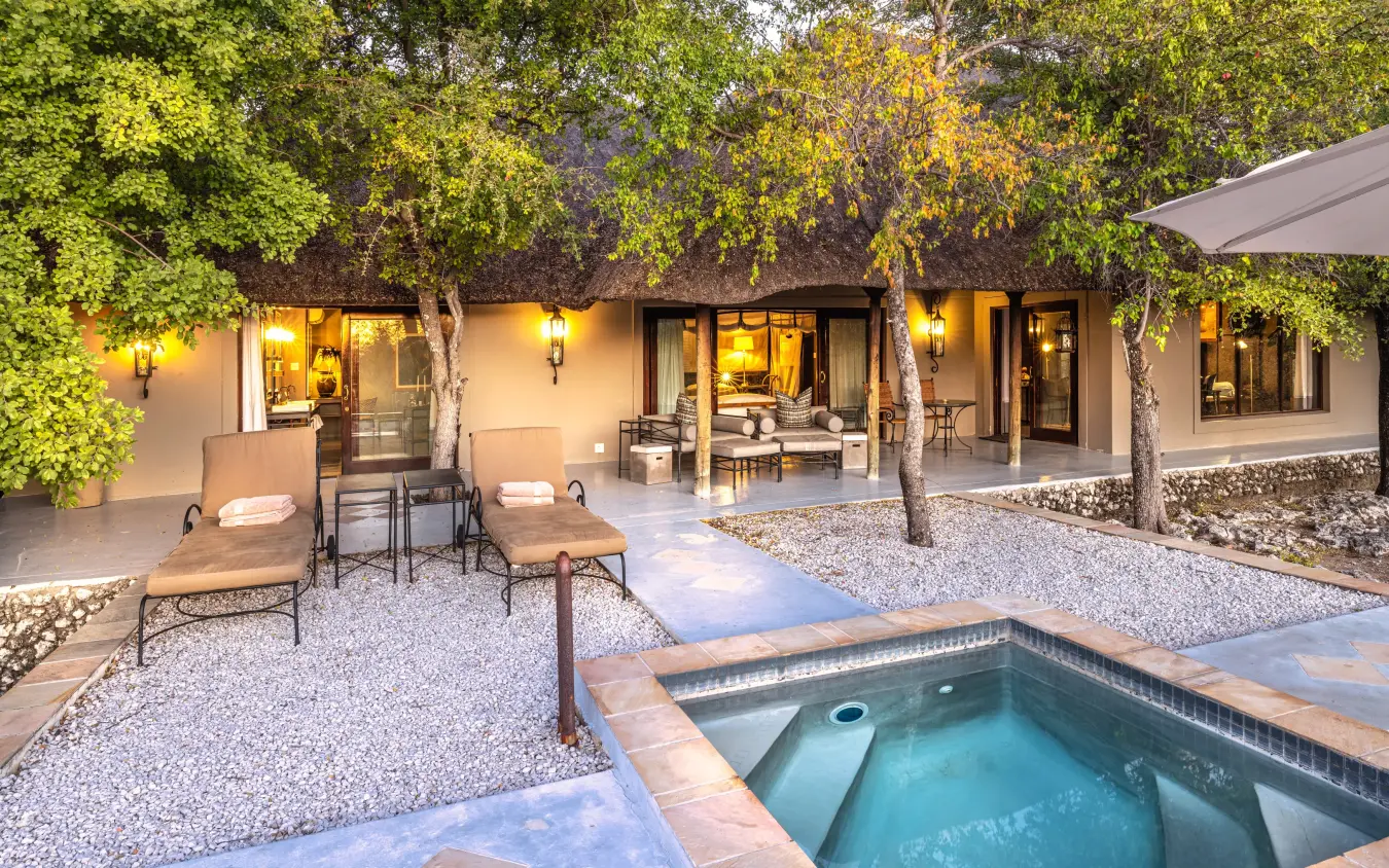 Spa pool and lounge area with trees and illuminated accommodation at dusk, Villa Mushara, Etosha National Park, Namibia