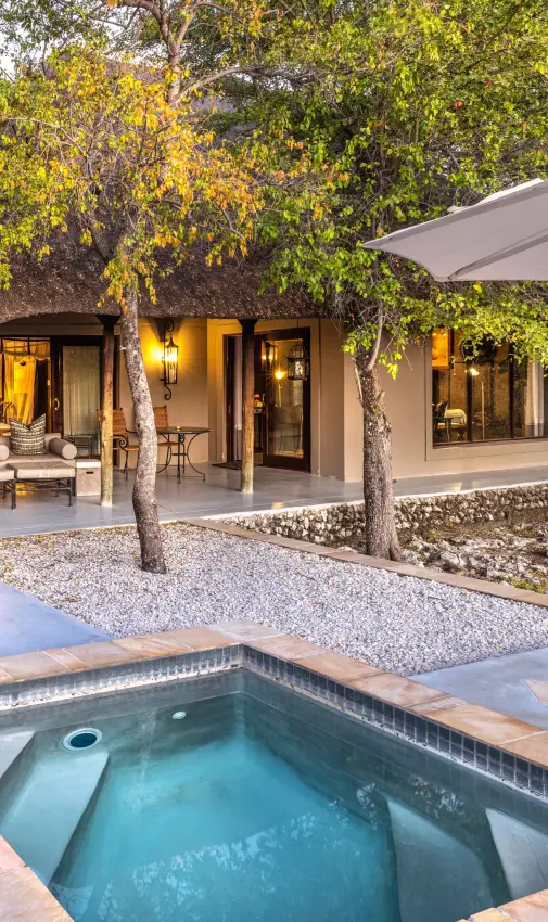 Spa pool and lounge area with trees and illuminated accommodation at dusk, Villa Mushara, Etosha National Park, Namibia