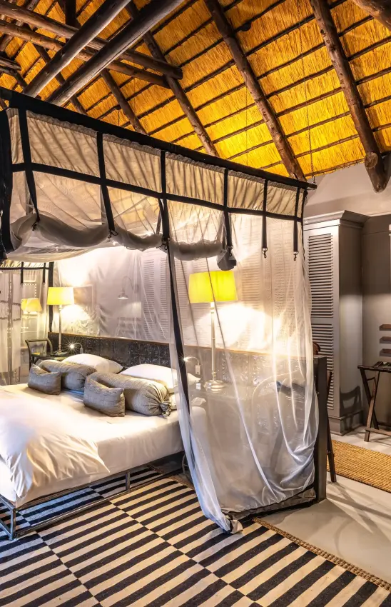 Four-poster bed with mosquito netting in thatched-roof bedroom, Villa Mushara, Etosha National Park, Namibia