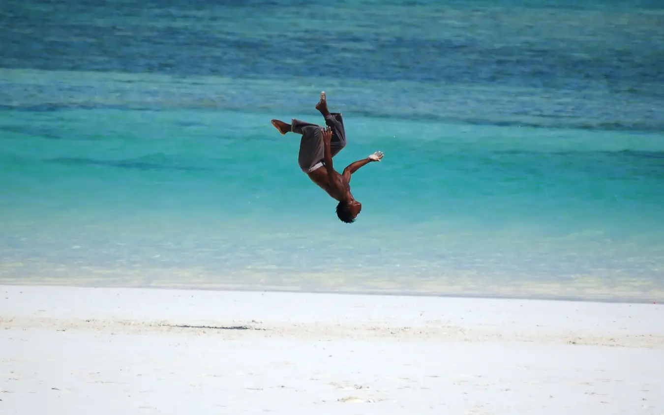 Person doing backflip into turquoise ocean water, Waterlovers Beach Resort, Diani Beach, Kenya