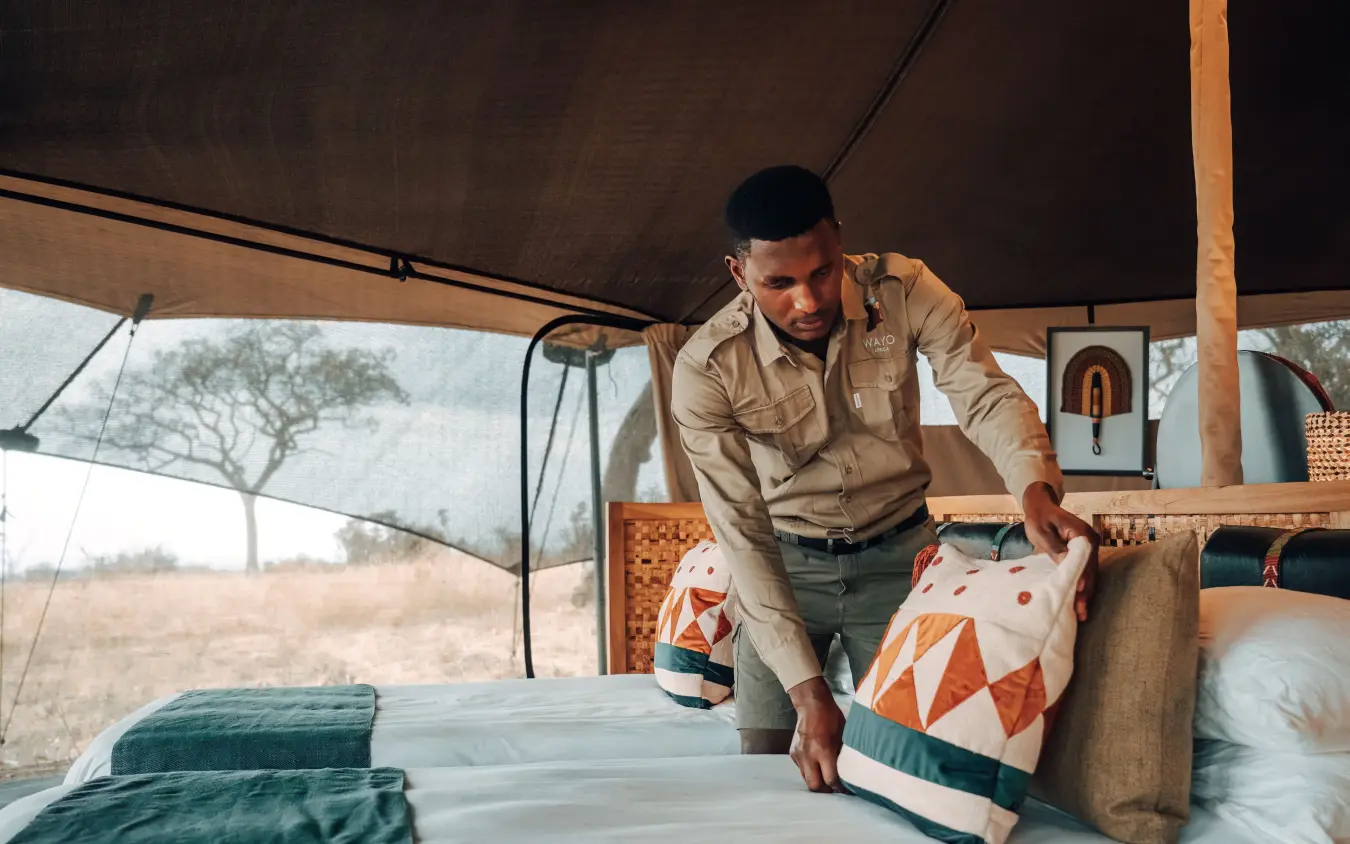 Staff member arranging bedding in safari tent interior, Serengeti Green Camp, Serengeti National Park, Tanzania