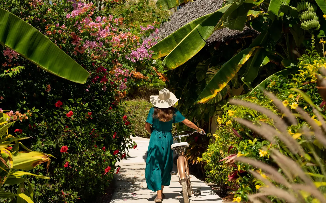 Woman walking bicycle through flowering garden pathway, White Sand Luxury Villas & Spa, Zanzibar & Pemba, Tanzania