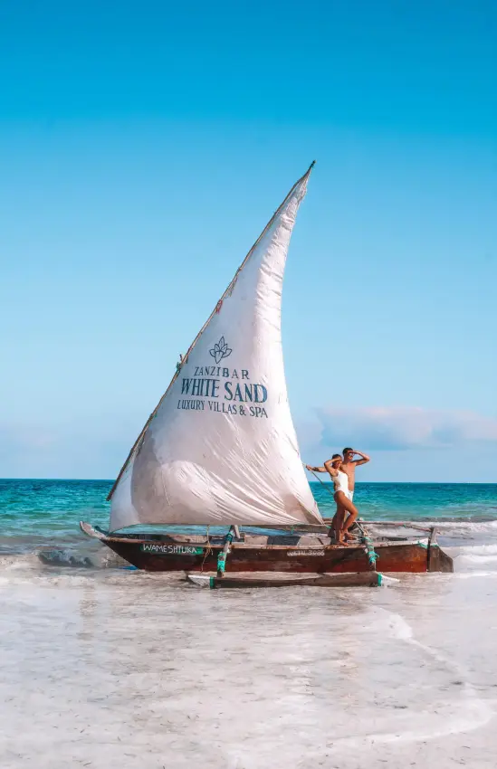 Man standing on traditional sailing dhow in shallow ocean waters, Zanzibar & Pemba, Tanzania