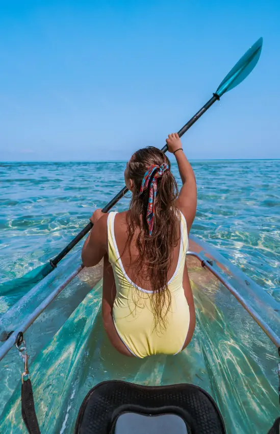 Woman kayaking in shallow turquoise water holding paddle, Zanzibar & Pemba, Tanzania