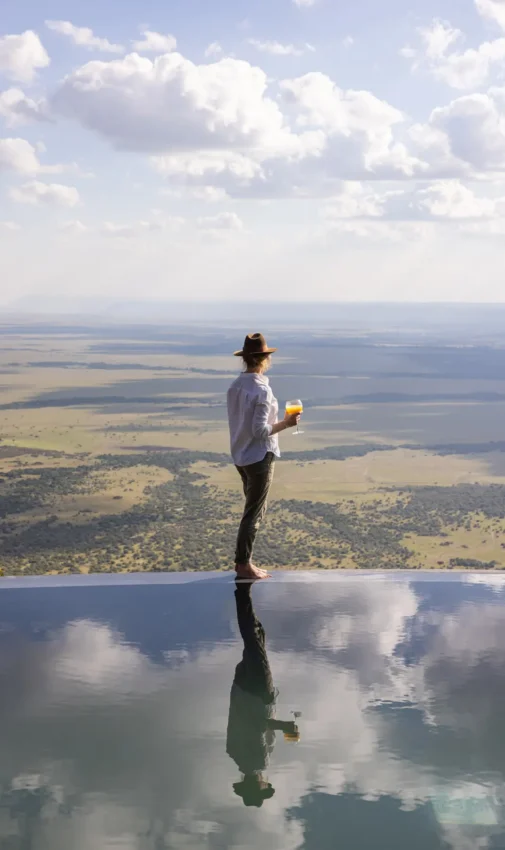 Man standing at infinity pool overlooking vast savanna landscape, Wild Hill, Maasai Mara, Kenya