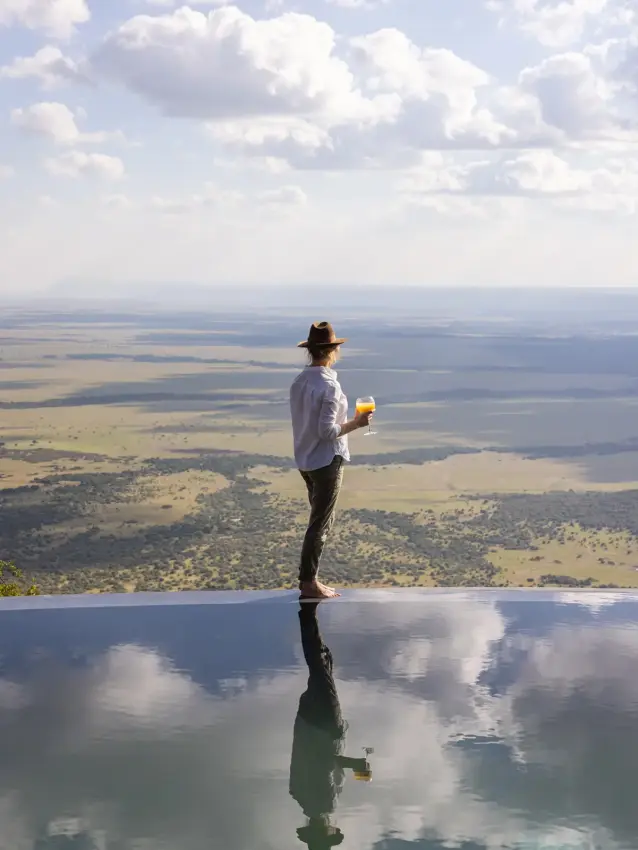 Man standing at infinity pool overlooking vast savanna landscape, Wild Hill, Maasai Mara, Kenya