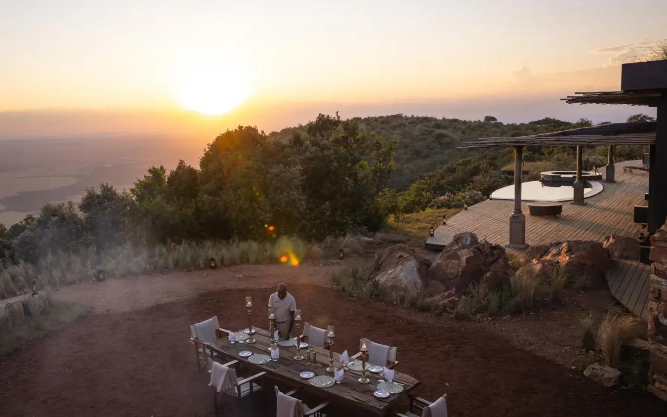 Outdoor dining table set at sunset overlooking valley, Wild Hill, Maasai Mara, Kenya