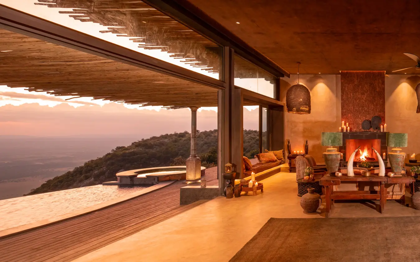 Modern lounge interior with fireplace overlooking valley at sunset, Wild Hill, Maasai Mara, Kenya