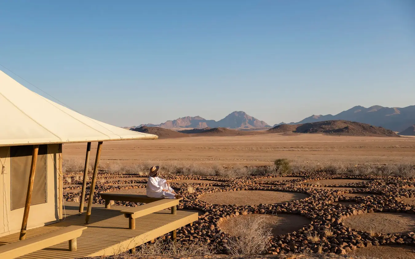 Guest relaxing on wooden deck overlooking desert landscape, Wolwedans Boulders Camp, NamibRand Private Reserve, Namibia
